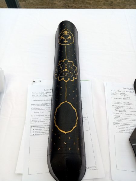 a black quiver decorated with gold lines, resting on some paper on a white table 